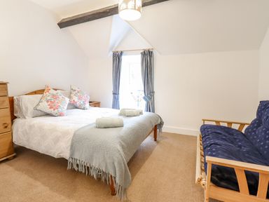 A bedroom with a bed with floral pillows a blue blanket towels and a blue futon sofa at Edrydd in Harlech