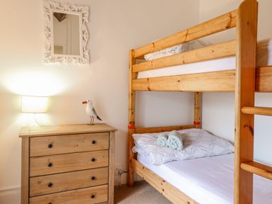 A bedroom with wooden bunk beds a wooden chest of drawers a lamp and a decorative bird at Edrydd in Harlech