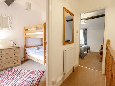View of a hallway with carpet leading to two bedrooms one with wooden bunk beds and a dresser the other with a bed and curtains at Edrydd in Harlech