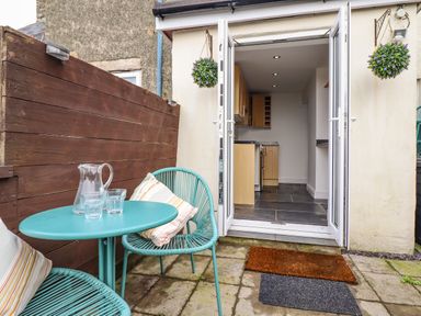 A small outdoor patio with a turquoise table and chairs and glassware opening into a kitchen at Edrydd in Harlech