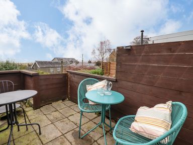A small outdoor patio with two turquoise chairs and a matching round table with a glass pitcher and two glasses at Edrydd in Harlech
