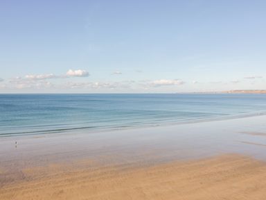 A sandy beach with calm waves and a person walking near the water at Onshore 7 in Newquay
