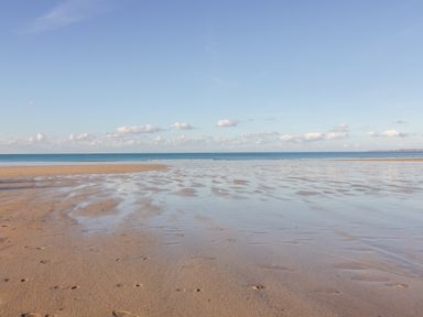 A sandy beach with wet patches and footprints by the sea under a blue sky at Onshore 7 in Newquay