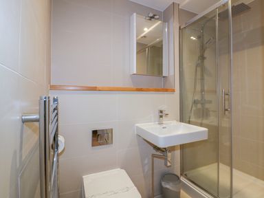 A bathroom with a wall-mounted sink a toilet a glass shower enclosure and a towel radiator at Onshore 7 in Newquay