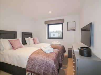 A bedroom with two single beds with folded towels on them a TV on a dresser and a window at Onshore 7 in Newquay