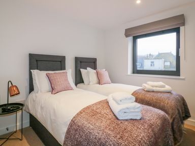 A bedroom with two single beds a side table with a lamp and a window at Onshore 7 in Newquay