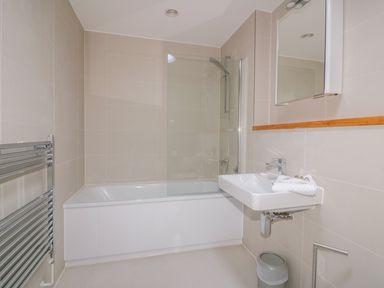 A bathroom with a bathtub shower combination a wall-mounted sink a mirror and a towel radiator at Onshore 7 in Newquay