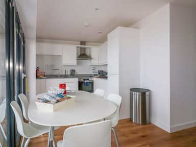 A kitchen with white cabinets a dining table with chairs and a stainless steel trash can at Onshore 7 in Newquay