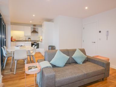 A modern living room with a gray sofa and two blue cushions next to a dining table and kitchen at Onshore 7 in Newquay