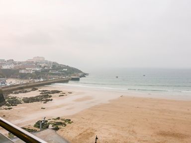 A beach with sand and rocks near a harbor wall with houses on a hill at Onshore 7 in Newquay