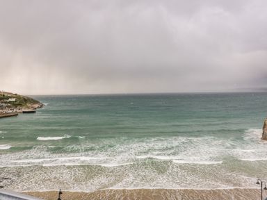 A view of the sea with waves and a sandy beach under a cloudy sky at Onshore 7 in Newquay