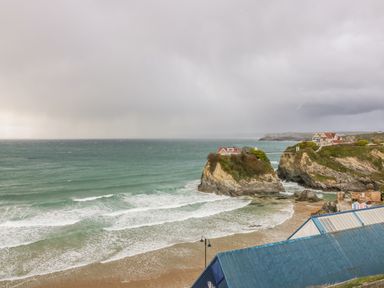 A coastal scene with a sandy beach waves cliffs and houses on rock formations at Onshore 7 in Newquay