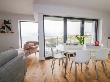 A dining area with a white table and chairs next to large windows overlooking the sea at Onshore 7 in Newquay