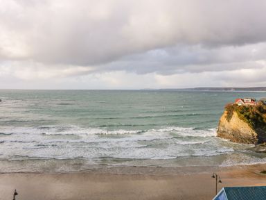 A beach with waves and a cliff with a house on top at Onshore 7 in Newquay