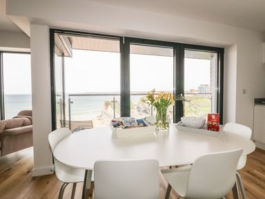 A dining area with a white table and chairs by large windows overlooking the sea at Onshore 7 in Newquay