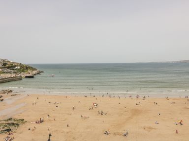 A sandy beach with people near the water and a coastal area with houses and a pier at Onshore 7 in Newquay