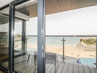 A balcony with a table and chairs overlooking a beach and ocean at Onshore 7 in Newquay