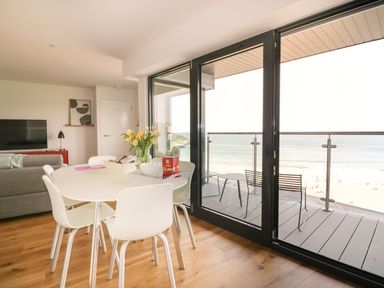 A dining area with white chairs and a round table next to glass doors opening to a balcony overlooking the beach at Onshore 7 in Newquay