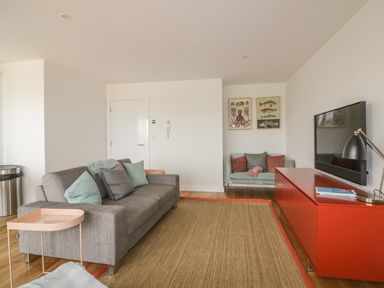 A living room with a grey sofa and a small turquoise couch a red cabinet with a tv and a lamp Onshore 7 Newquay