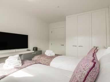 A bedroom with two beds white linens purple pillows and a wall mounted tv at Onshore 7 in Newquay