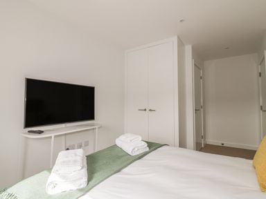 A bedroom with a bed covered in white linen and green throw facing a wall-mounted TV and white double door closet at Onshore 7 in Newquay