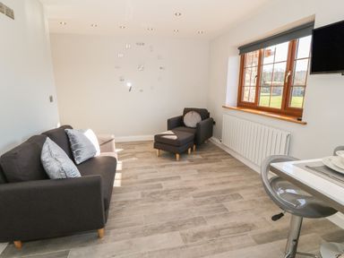 A sitting area with a sofa armchair and ottoman near a window and a wall clock at Afon Rhos Bach in Llanrug