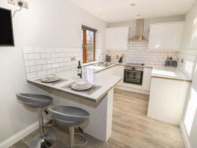 A kitchen with white cabinets a stove a sink and two gray bar stools at Afon Rhos Bach in Llanrug