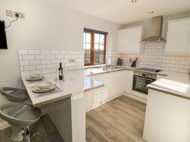 A kitchen with white cabinets a window and a breakfast bar with two stools at Afon Rhos Bach in Llanrug