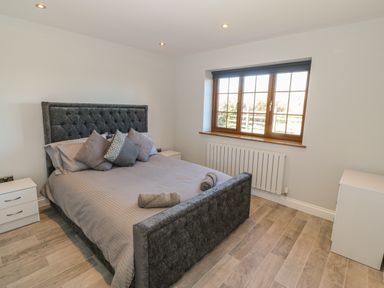 A bedroom with a large bed pillows beside windows and white bedside tables at Afon Rhos Bach in Llanrug