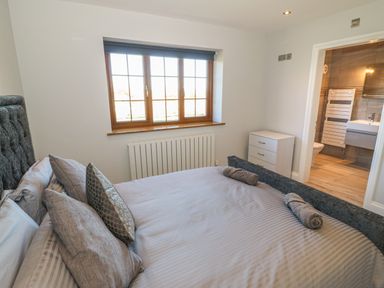 A bedroom with a bed pillows window with blinds white dresser and an en suite bathroom at Afon Rhos Bach in Llanrug