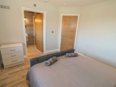 A bedroom with a bed and rolled towels two wooden doors and a white dresser at Afon Rhos Bach in Llanrug