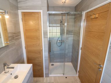 A bathroom with a shower enclosure a sink and two wooden doors at Afon Rhos Bach in Llanrug
