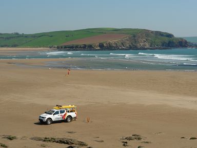 A lifeguard vehicle on a sandy beach with ocean waves and green hills in the background at Duffield in St Ann's Chapel