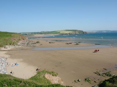 A sandy beach with people sunbathing and windsurfing by grassy cliffs and hills at Duffield in St Ann's Chapel