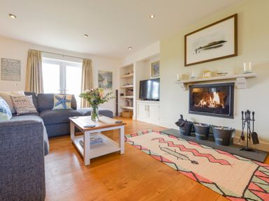 A living room with a blue sofa a wooden coffee table with flowers a wall-mounted fireplace and a TV at Duffield in St Ann's Chapel