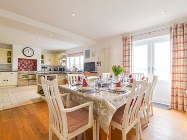 A dining table set with plates glasses and napkins in a room with kitchen cabinets and a clock on the wall at Duffield in St Ann's Chapel