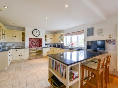 A kitchen with cream cabinets black countertops and a clock above the stove with bar stools at Duffield in St Ann's Chapel