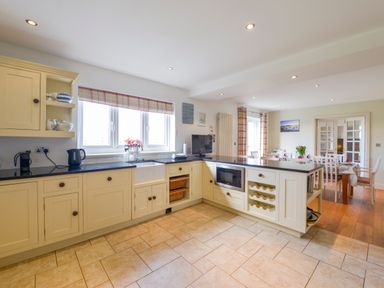 A kitchen with cream cabinets a black countertop a window above a sink and a dining table in the background at Duffield in St Ann's Chapel