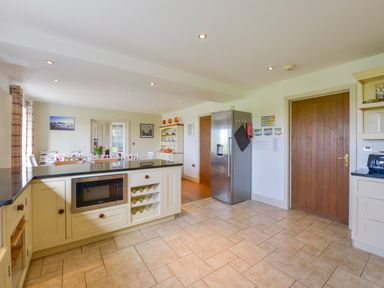 A kitchen with an island, stainless steel refrigerator, wooden doors, and a dining area with chairs and a table at Duffield in St Ann's Chapel