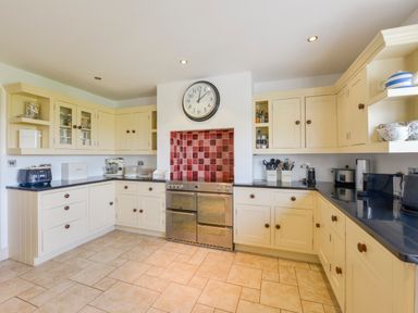 A kitchen with cream cabinets black countertops stainless steel oven and a wall clock at Duffield in St Ann's Chapel
