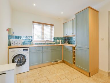 A kitchen with blue cabinets a washing machine tiled floor and a window with blinds at Duffield in St Ann's Chapel