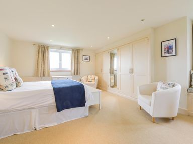 A bedroom with a bed a window with curtains two white armchairs and a large wardrobe with mirrored doors at Duffield in St Ann's Chapel
