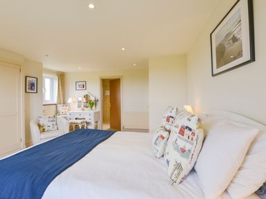 A bedroom with a bed blue throw pillows a white desk with a mirror and flowers and a white armchair at Duffield in St Ann's Chapel