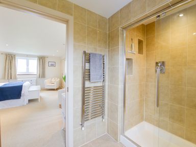 A bathroom with a tiled shower and heated towel rail next to a bedroom with a bed chair and window at Duffield in St Ann's Chapel