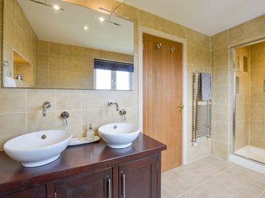 A bathroom with two white sinks on a dark wooden counter a large mirror a wooden door a towel rack and a shower at Duffield in St Ann's Chapel
