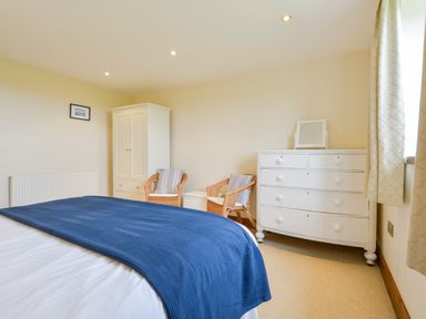 A bedroom with a bed covered by a blue blanket two wicker chairs a white wardrobe and a white chest of drawers at Duffield in St Ann's Chapel