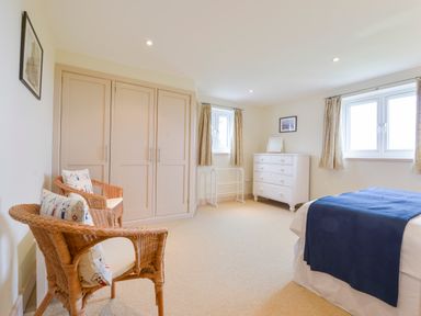 A bedroom with two wicker chairs cushions wardrobe white dresser two windows and a bed with a blue blanket at Duffield in St Ann's Chapel