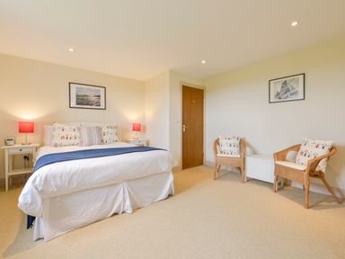 A bedroom with a double bed flanked by two bedside tables with lamps and two wicker chairs with cushions near a wooden door at Duffield in St Ann's Chapel