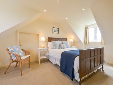A bedroom with a wooden bed frame white bedside tables lamps a wicker chair and a window at Duffield in St Ann's Chapel