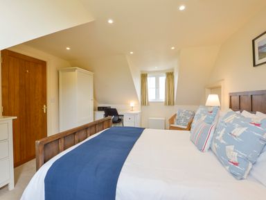 A bedroom with a wooden bed with blue and white pillows a wooden door a white wardrobe a desk with a chair and lamp and a window with curtains at Duffield in St Ann's Chapel